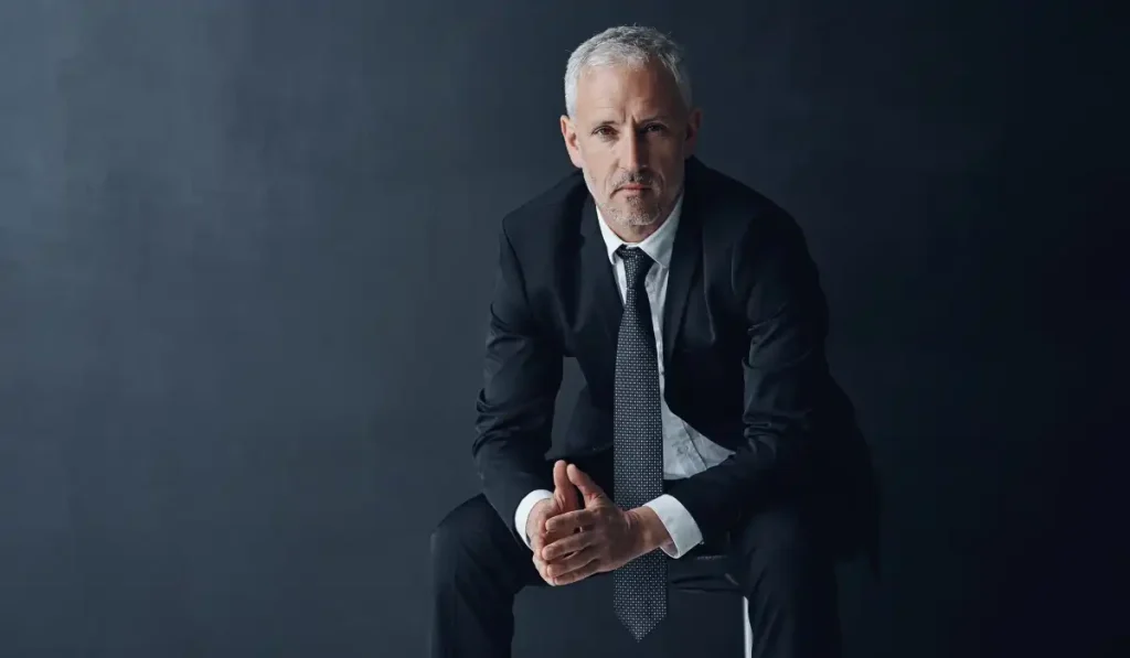 a person sitting on a chair wearing a suait in front of a black background