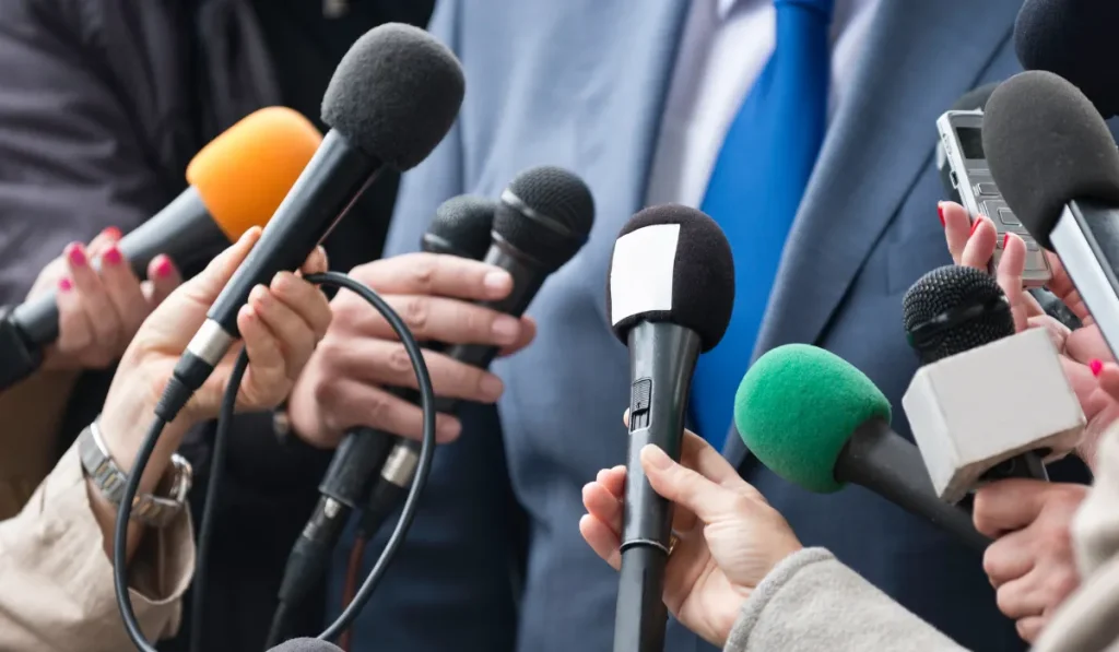 multiple mics are pointed at a person wearing a blue suit and a tie