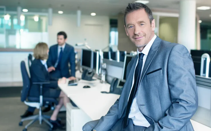 CEO seated at a desk in a modern corporate office, with two executives collaborating in the background.