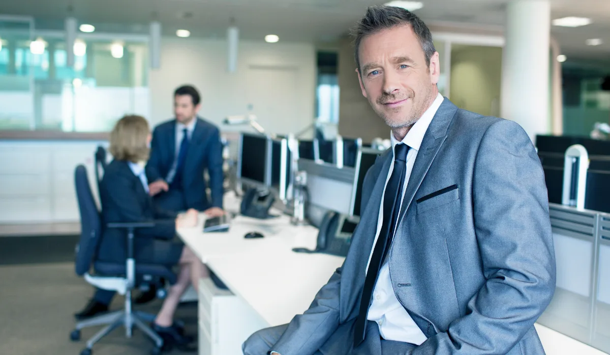 CEO seated at a desk in a modern corporate office, with two executives collaborating in the background.