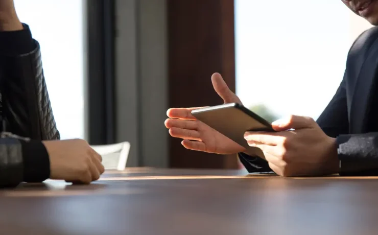 a person holding a tablet screen speaking to another person in an office