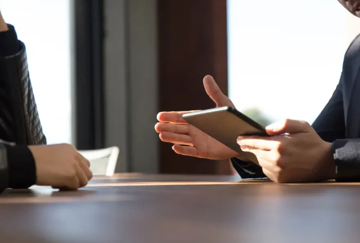 a person holding a tablet screen speaking to another person in an office