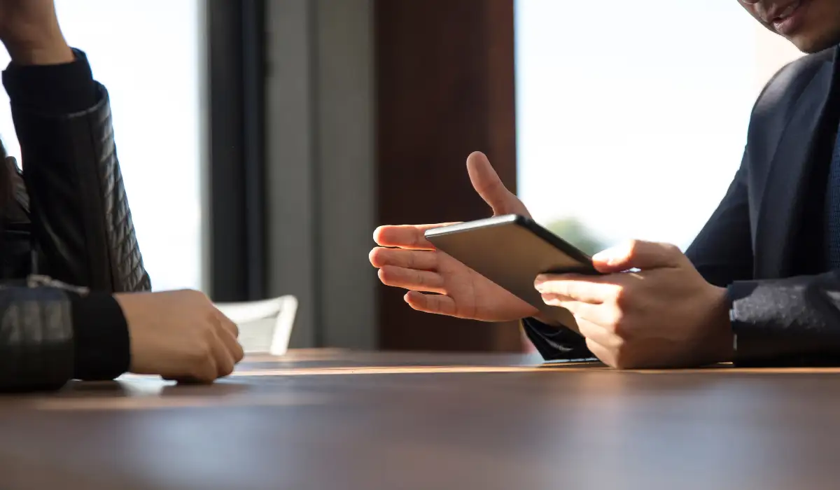 a person holding a tablet screen speaking to another person in an office
