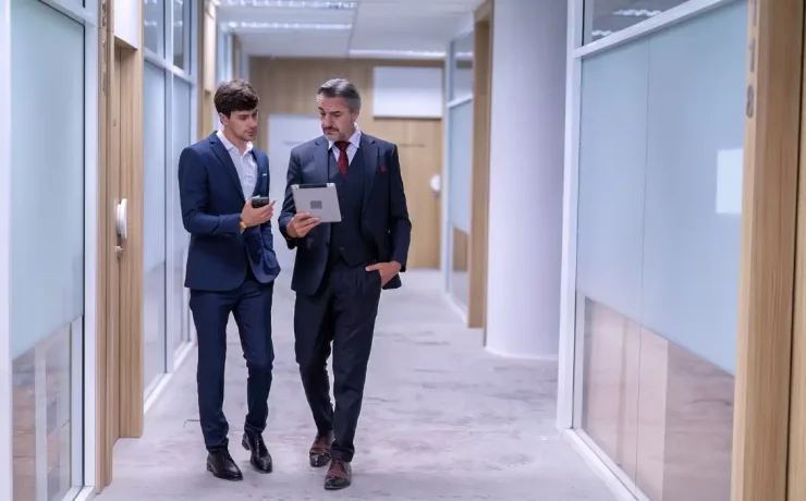 Assistant shows information on a tablet to a CEO while they walk through an office lobby