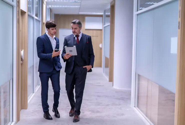 Assistant shows information on a tablet to a CEO while they walk through an office lobby