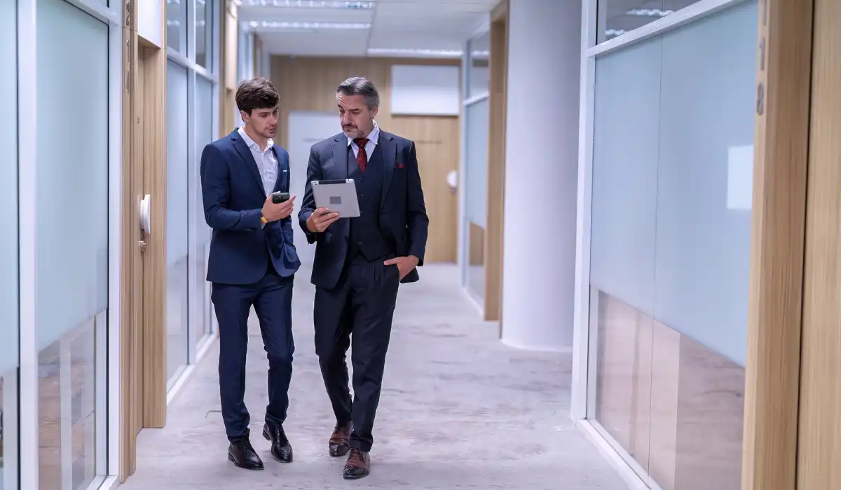 Assistant shows information on a tablet to a CEO while they walk through an office lobby